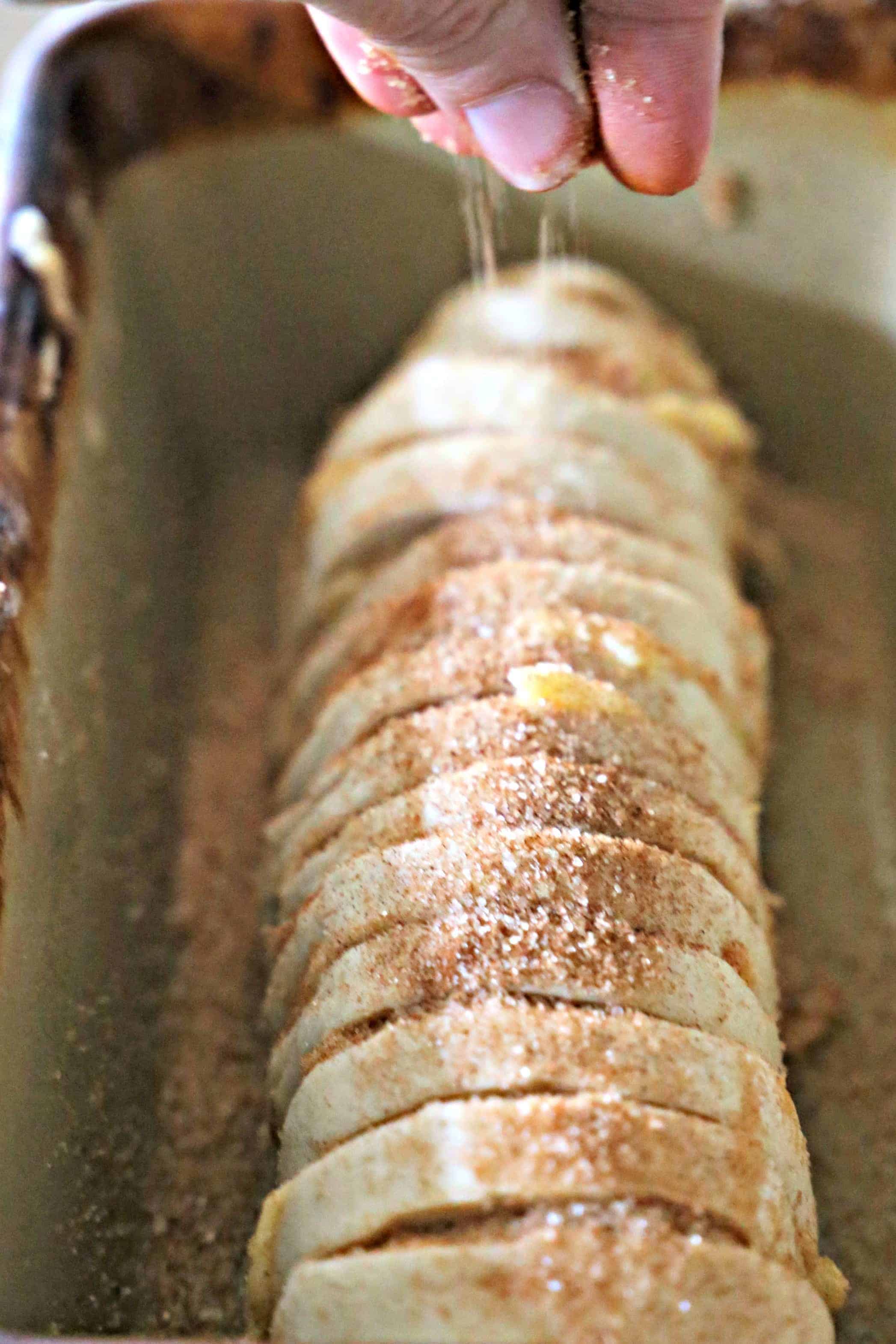 Sprinkling sugar over loaf of bread.