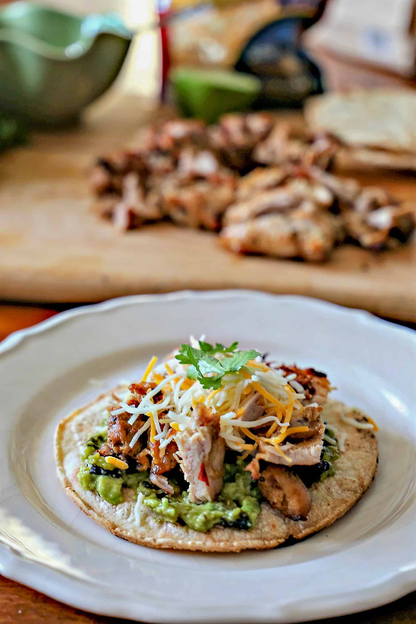 Grilled Chicken Tostadas with homemade guacamole, cheese, and cilantro on a plate.