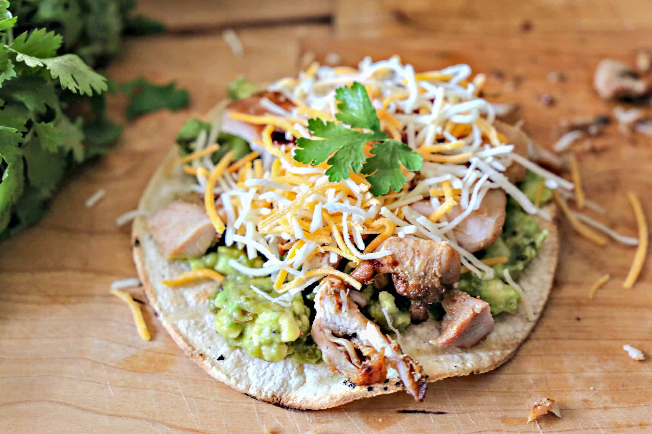 Chicken tostada topped with guacamole and cheese.