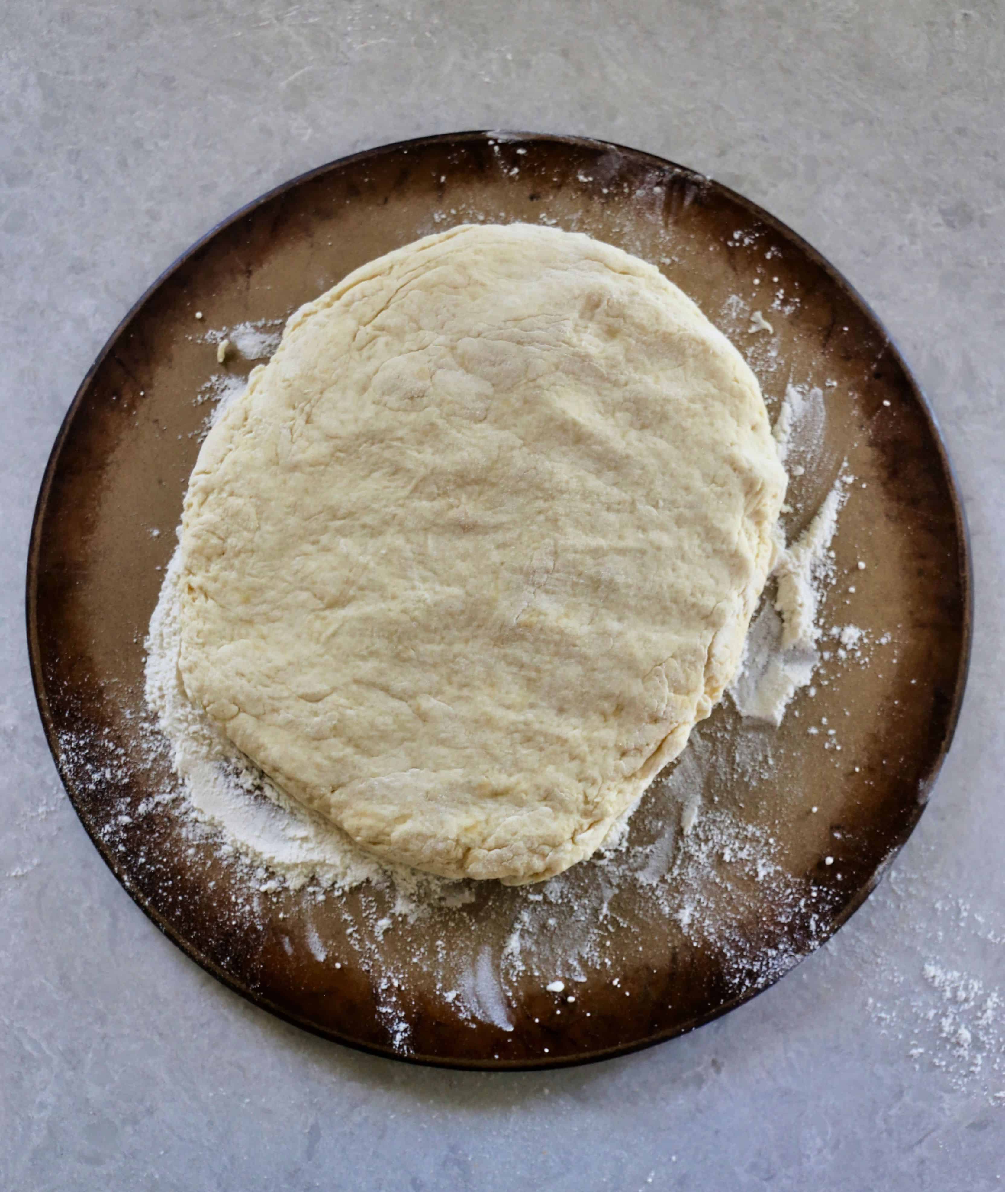 Biscuit dough patted out into a circle on a baking stone.