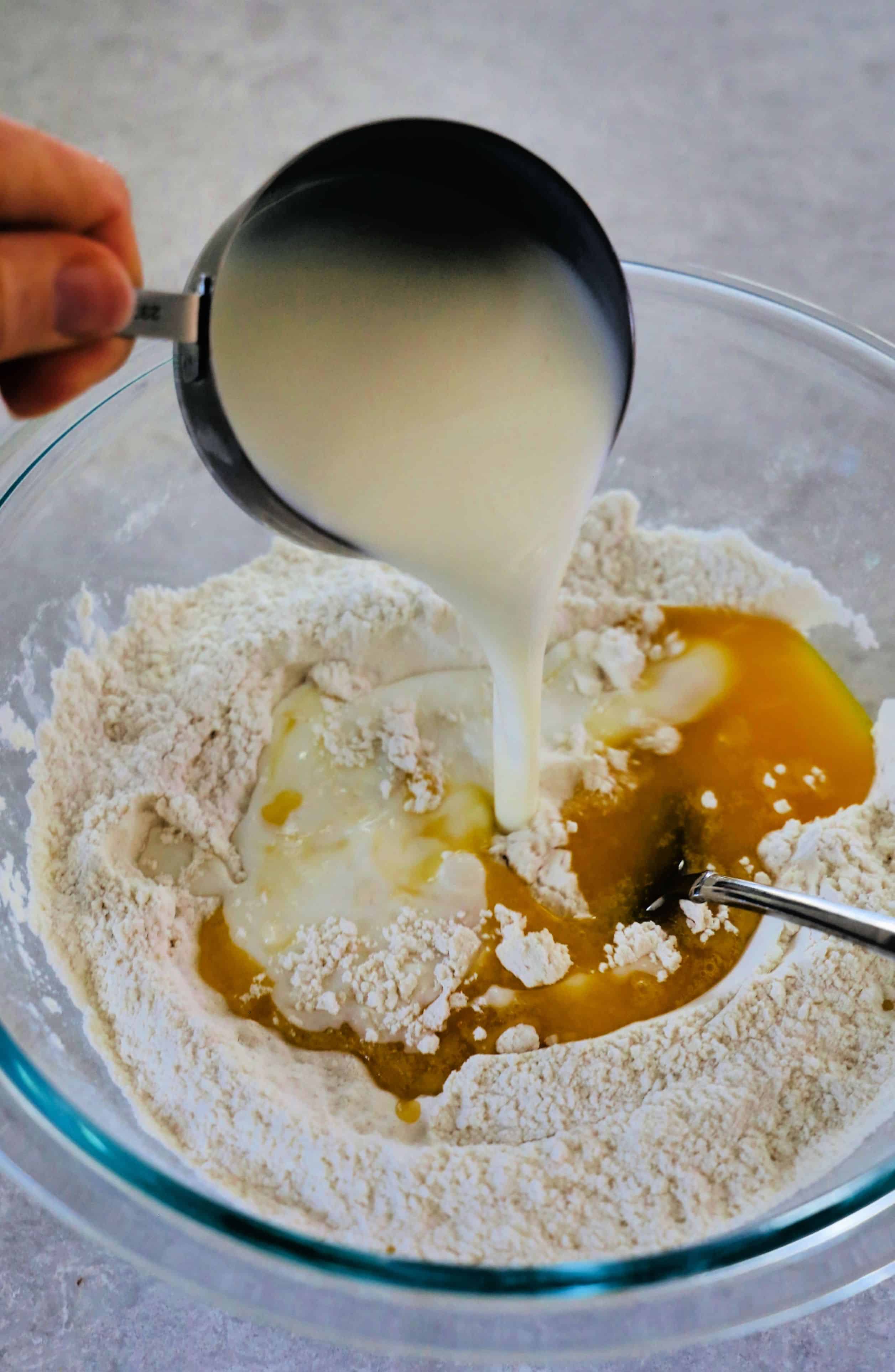 Pouring buttermilk into flour mixture to make biscuits.