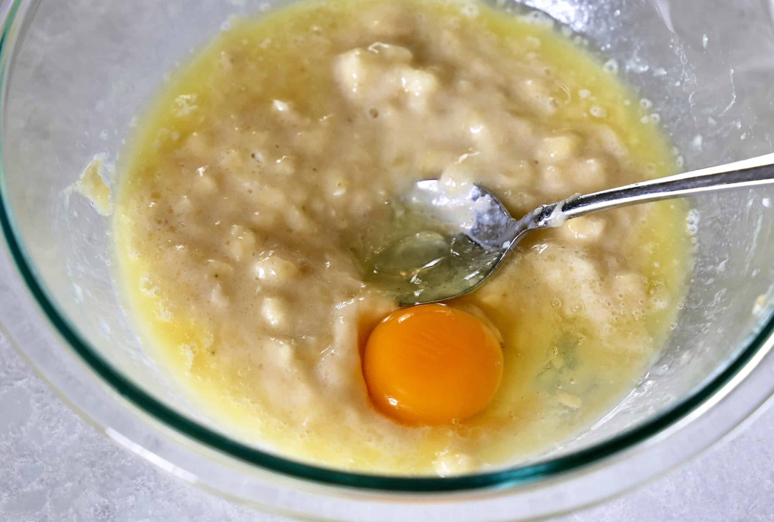 Mashed bananas and egg in a glass mixing bowl.
