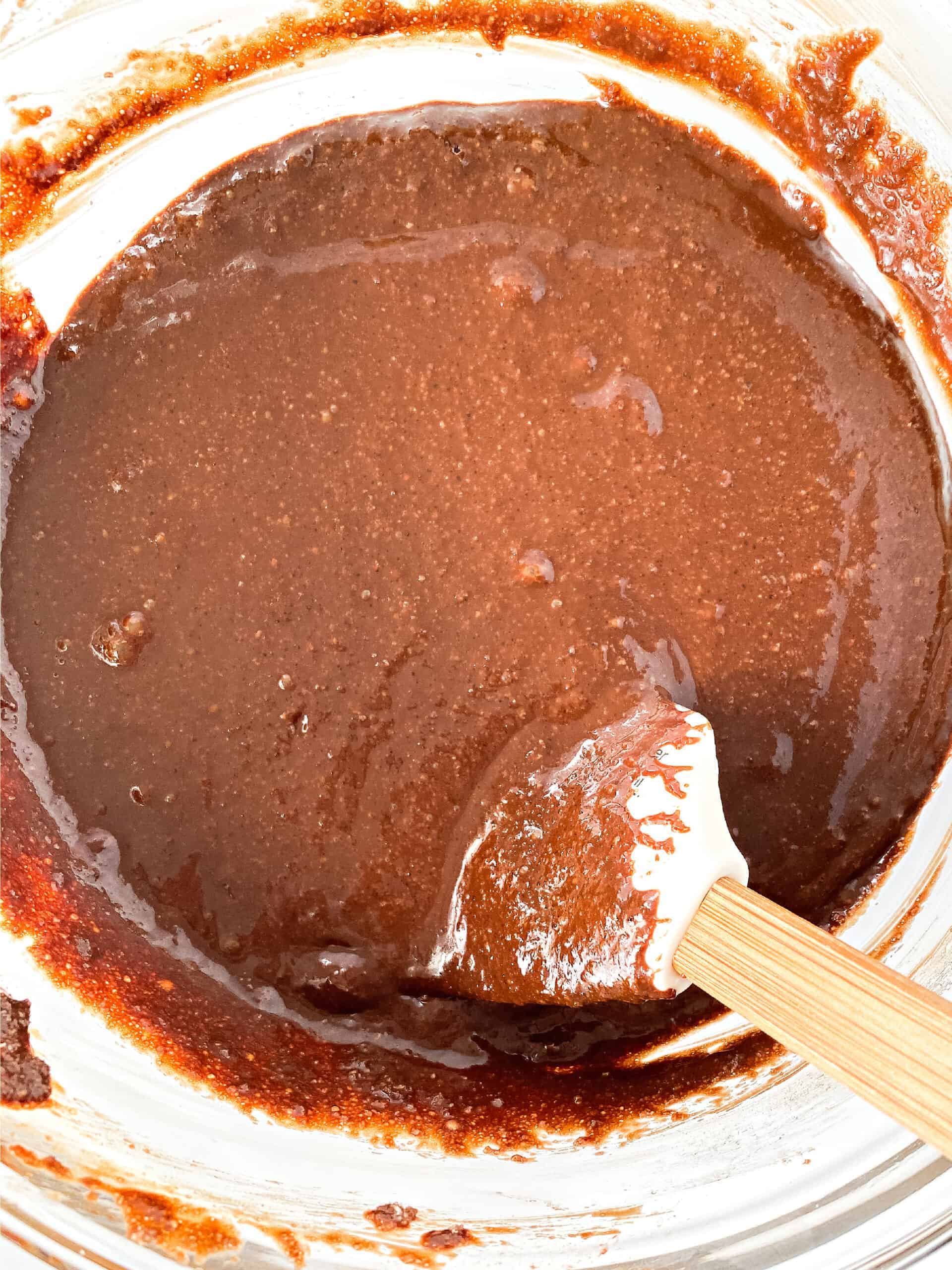 Spatula stirring brownie batter in a glass mixing bowl.