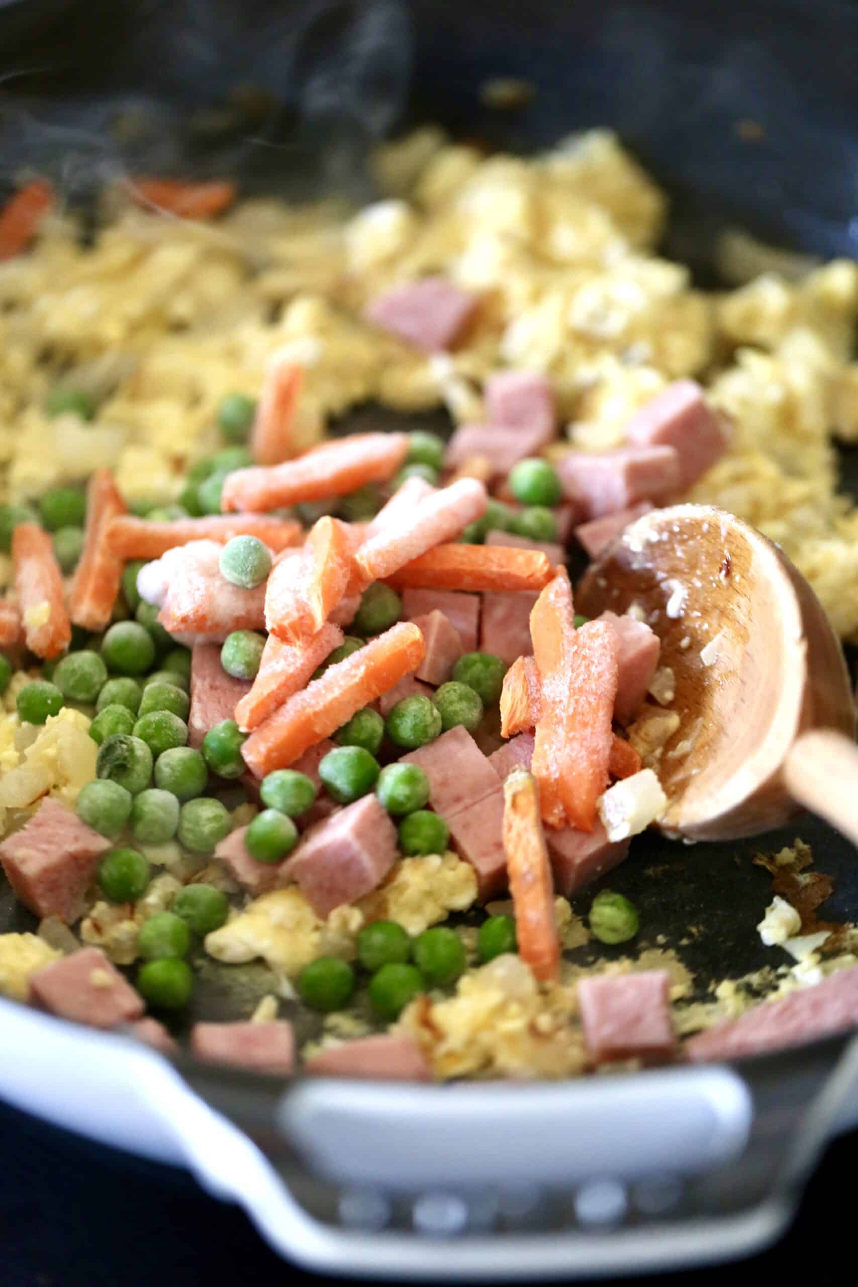 Frozen vegetables being added to fried rice.