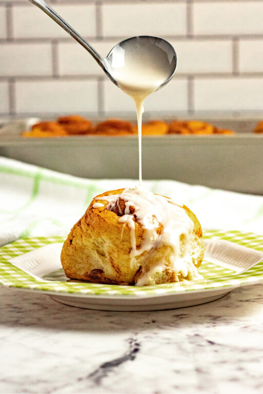 drizzling icing on top of a cinnamon roll