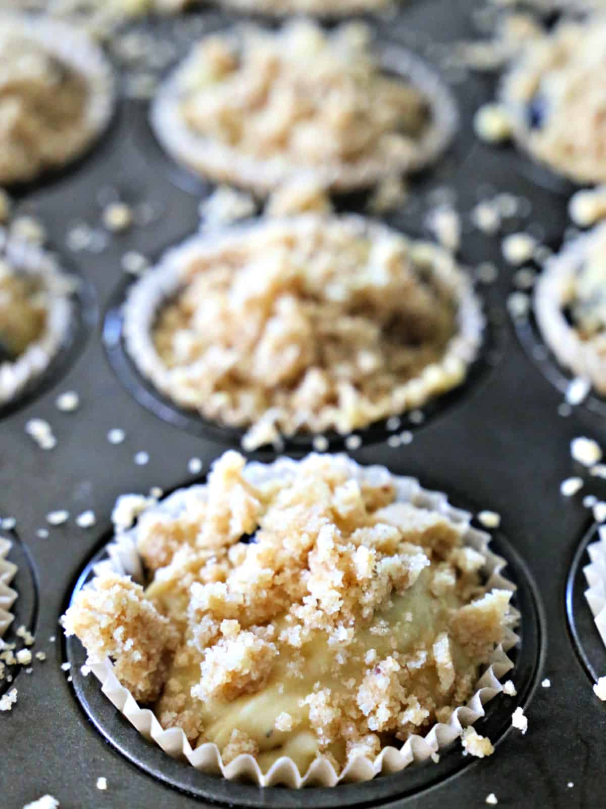 Bakery-Style Blueberry Muffins - there's no need to go to the bakery with this easy recipe. Unbaked blueberry muffins with crumb topping in a muffin pan.