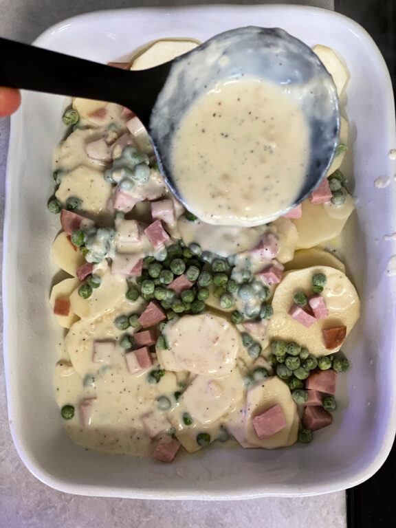spooning roux over potatoes, ham, and peas