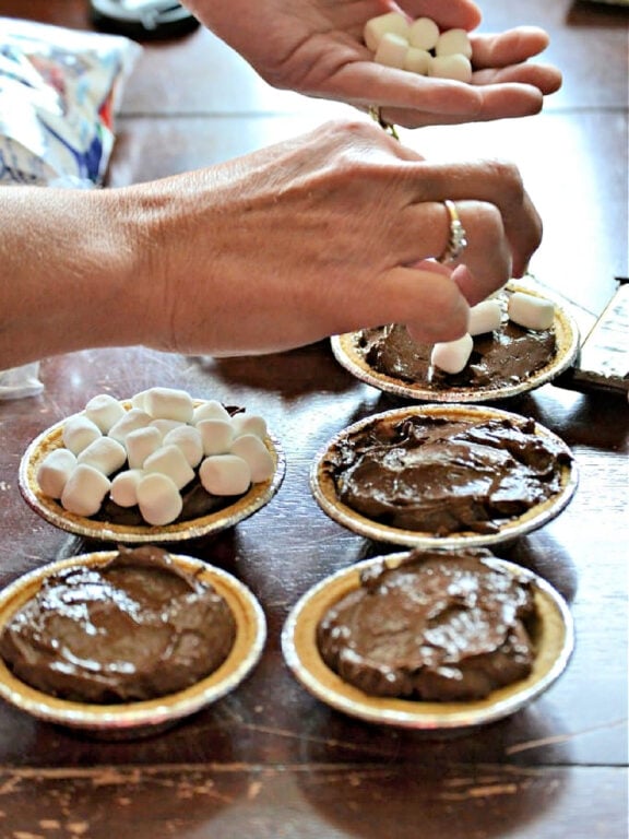 Placing marshmallows on top of rich, chocolaty pudding to make s'more pies topping chocolate pies with marshmallows