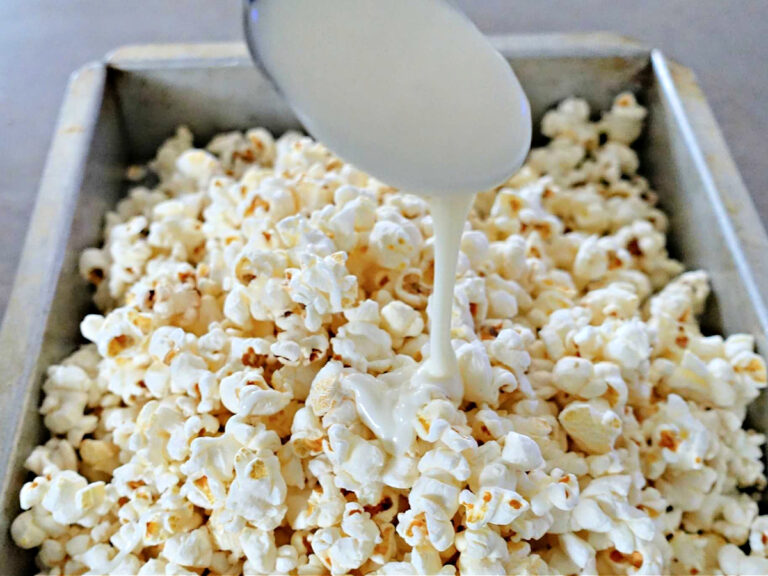 Funfetti Popcorn pouring almond bark on top of pop corn