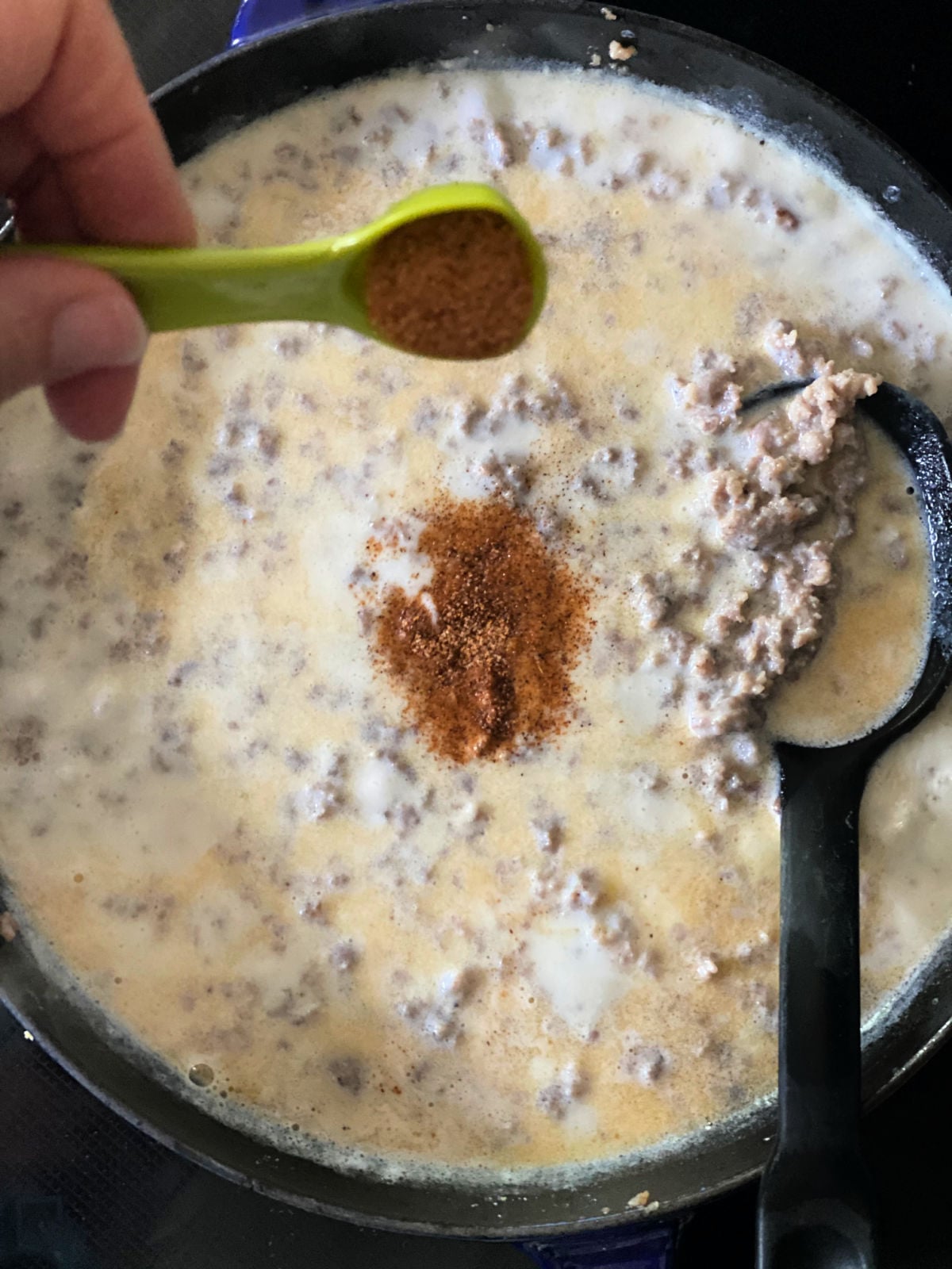 Cajun seasoning being added to sausage gravy in a skillet.