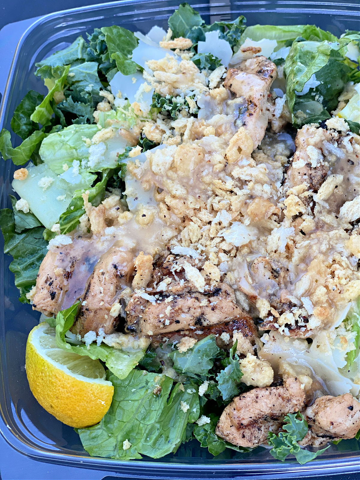 Bowl of Chick-fil-A's lemon kale salad with bed of greens, chicken, and lemon wedge.