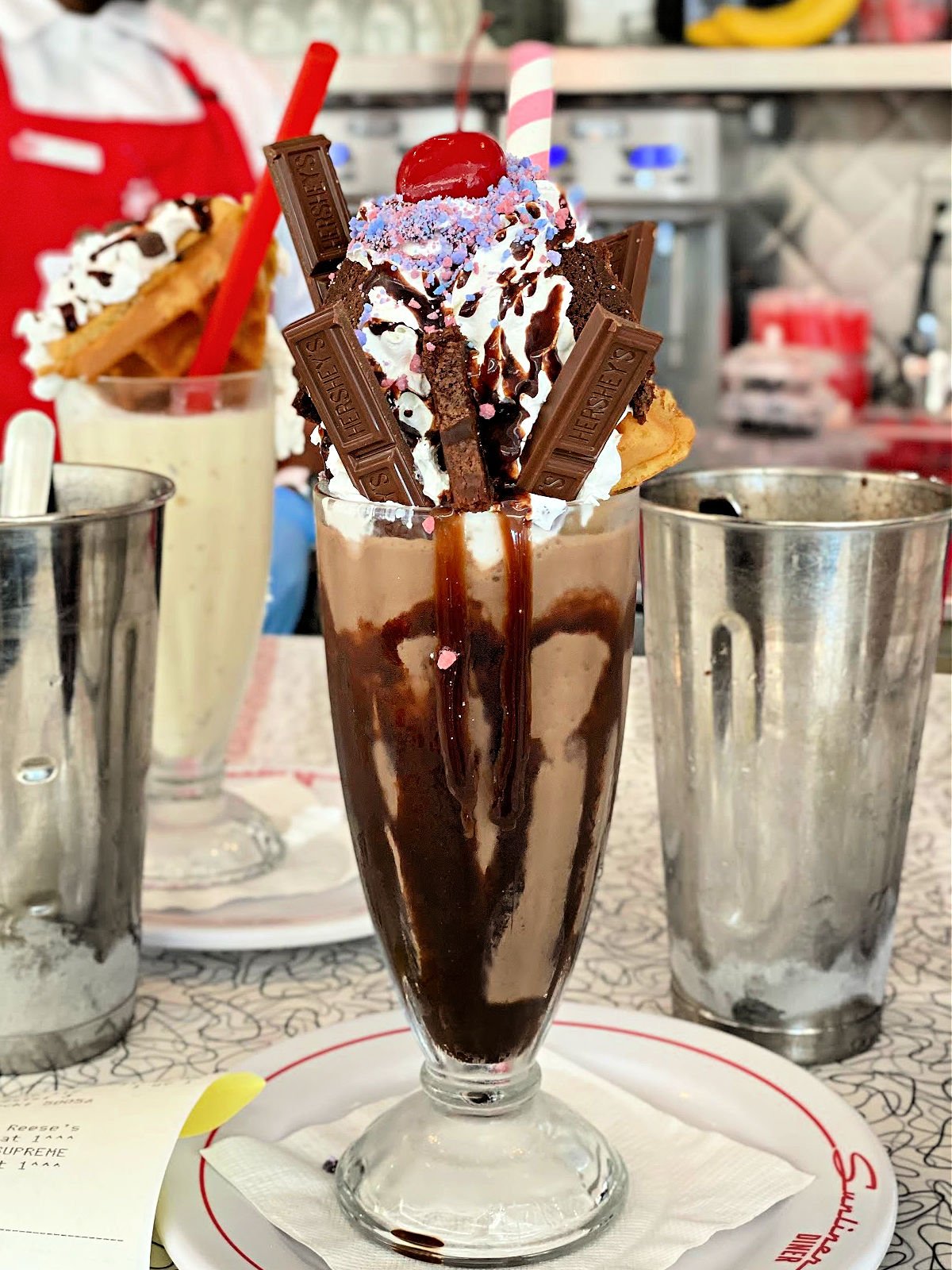 Chocolate milkshake loaded with chocolate bars, whipped cream, and sprinkles.