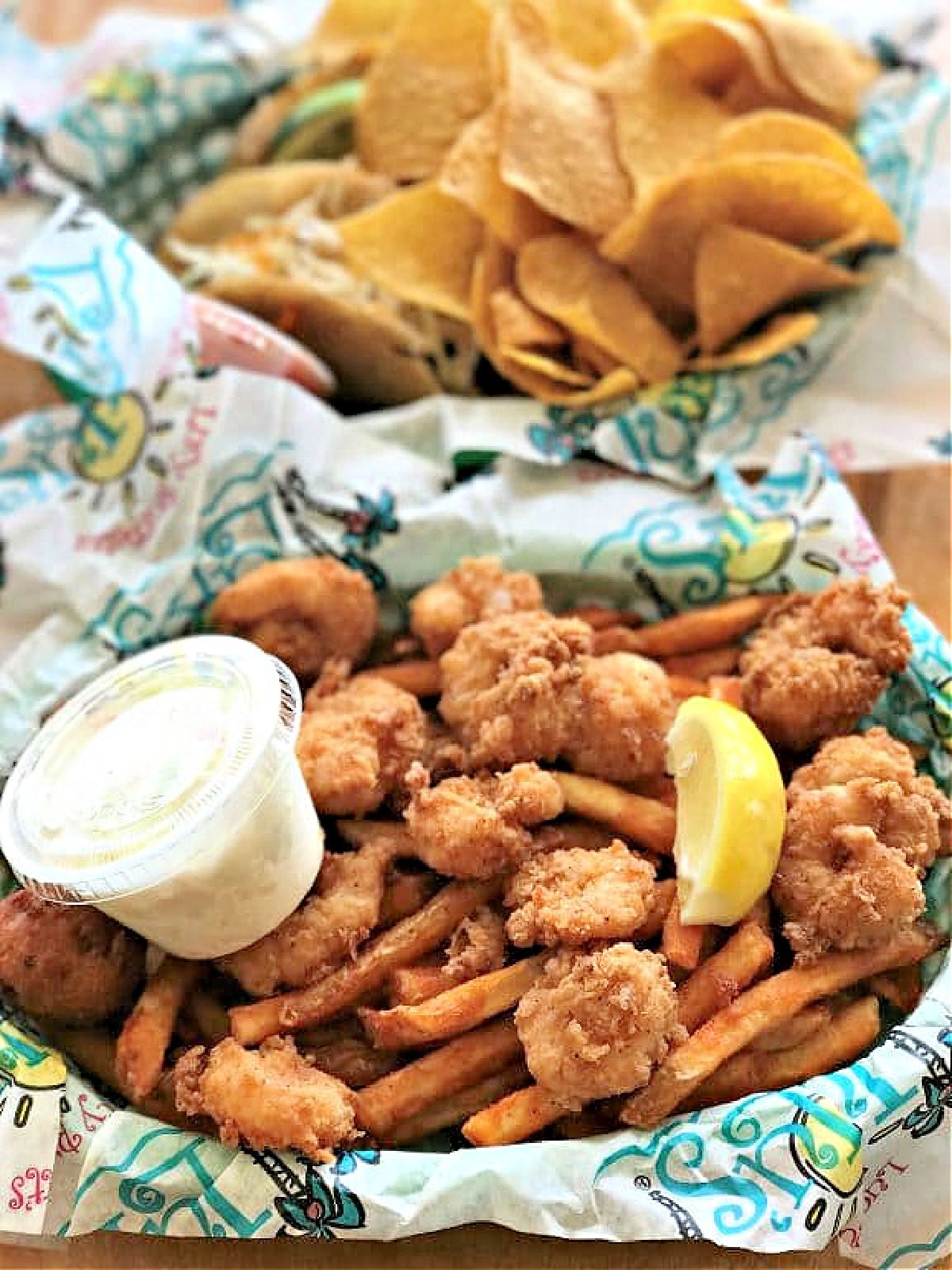 A basket of fried shrimp and French fries and slice of lemon.