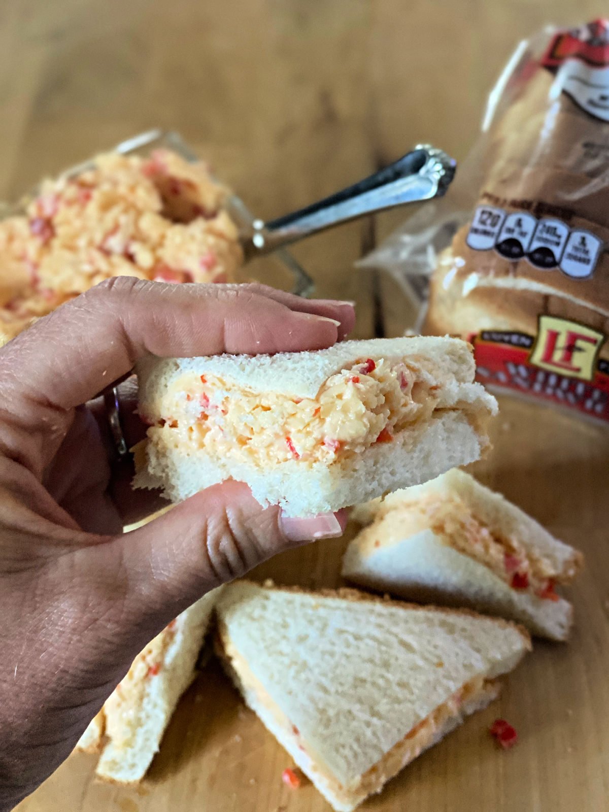 Village Tavern's Pimento Cheese Woman holding a slice of homemade pimento cheese sandwich.