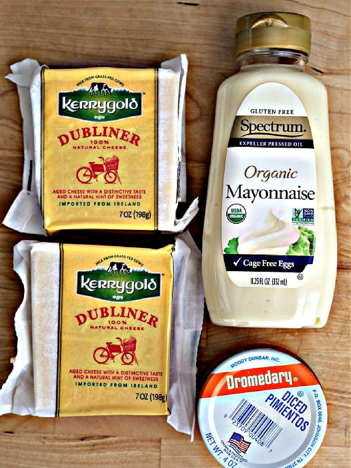 Village Tavern's Pimento Cheese Recipe Kerrygold Dubliner cheese, mayonnaise, and diced pimentos on a cutting board.