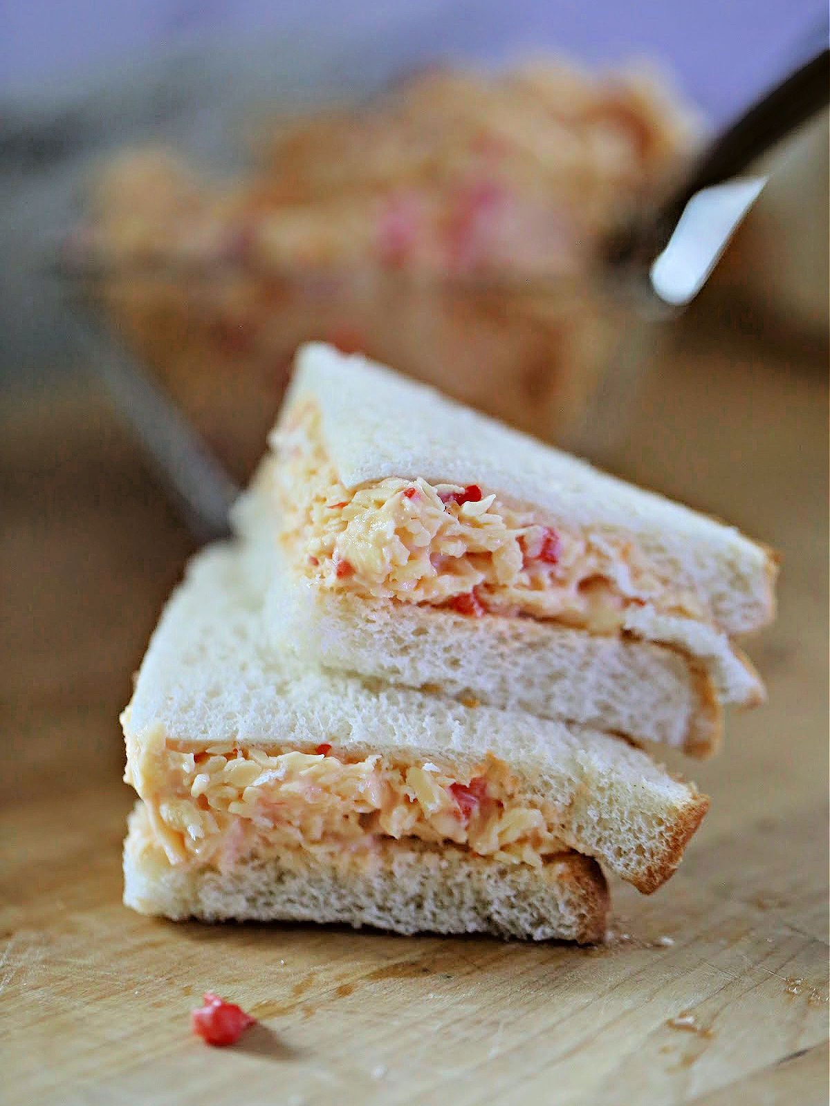 Pimento cheese sandwich slices stacked on top of each other on a cutting board.