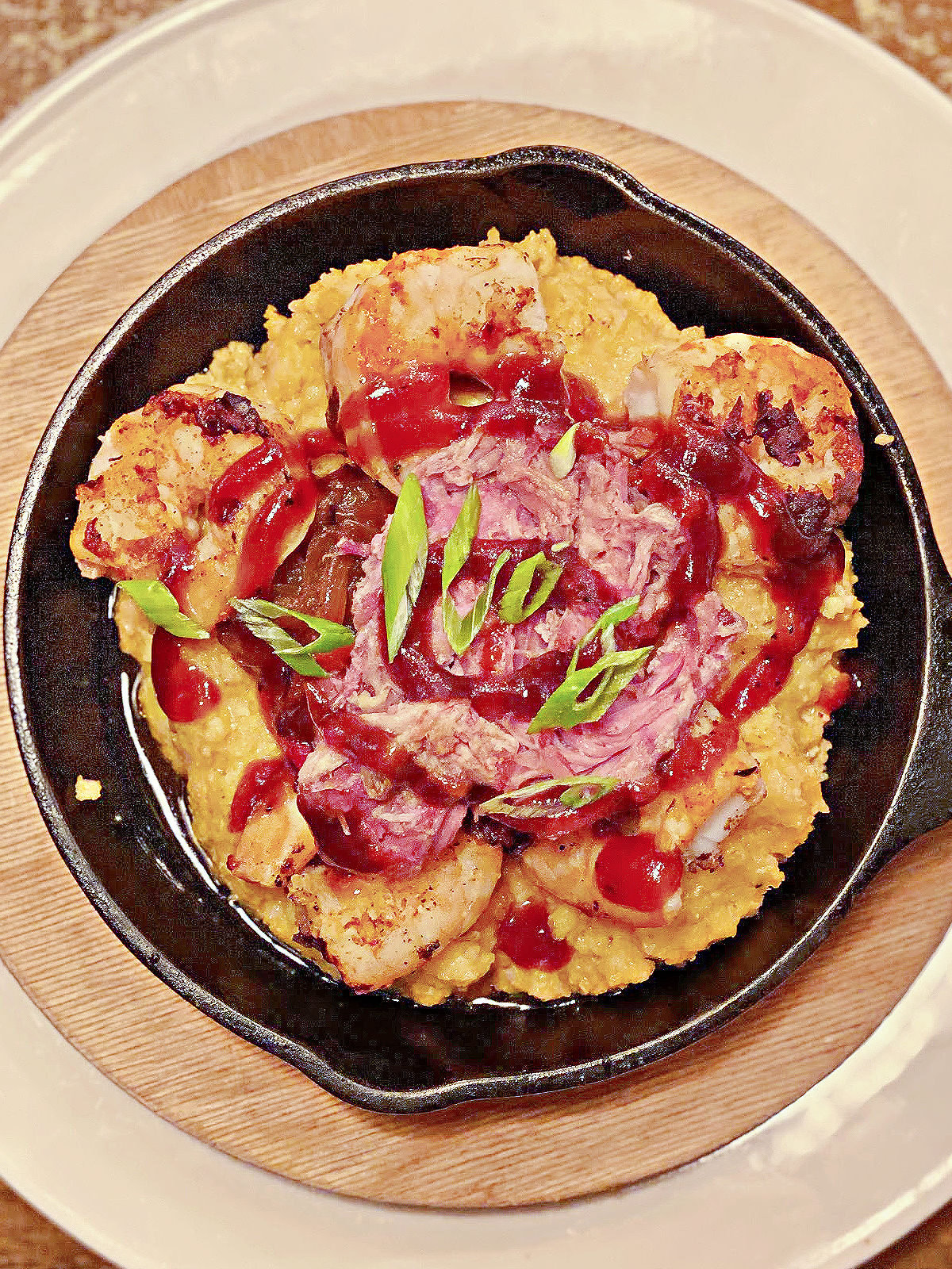 Small cast iron skillet of grits topped with shrimp and drizzled with bbq sauce.