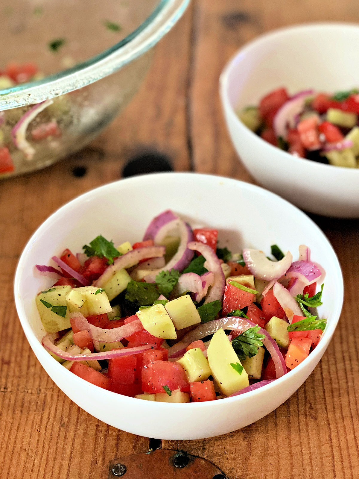 Bowl of tomato cucumber salad made with red onions, tomatoes, cucumber, and cilantro.