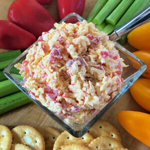Pimento cheese in a glass dish surrounded by veggies and crackers.