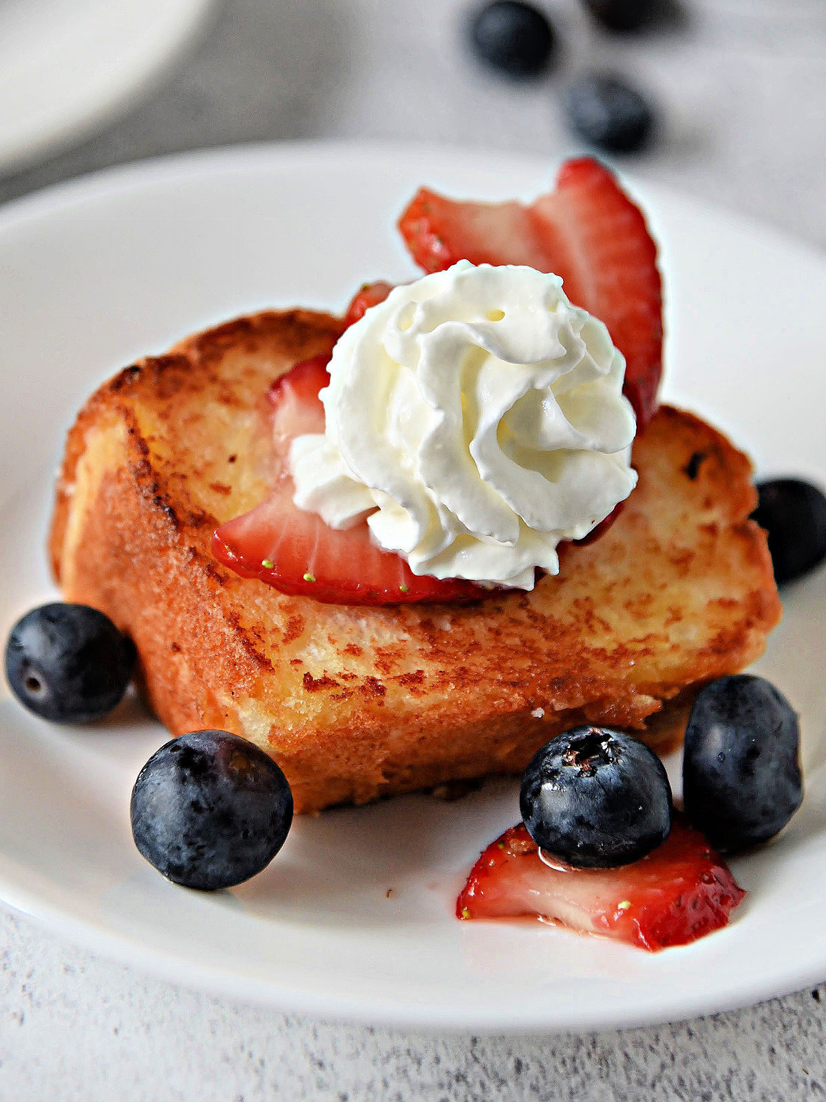 Slice of toasted angel food cake on a white plate with blueberries and strawberries.