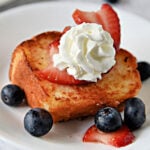 Slice of toasted angel food cake on a white plate with blueberries and strawberries.