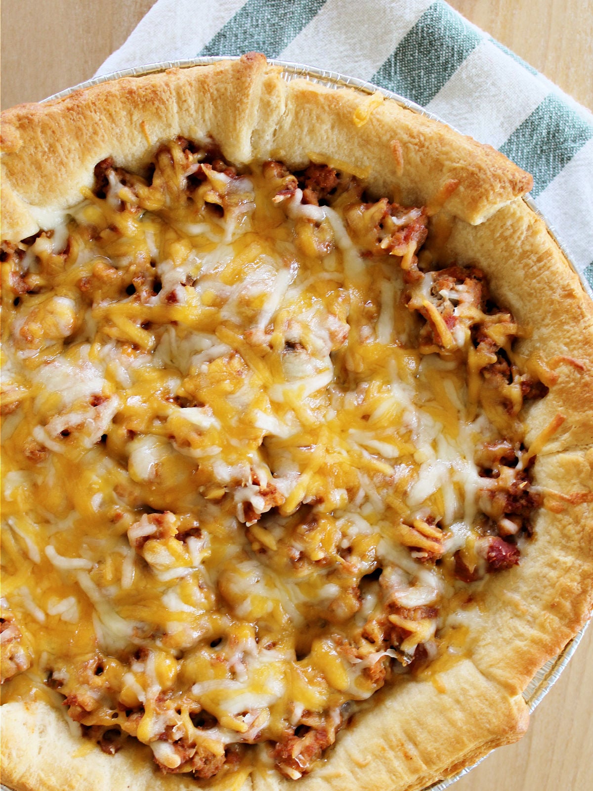 Taco pie topped with cheese on a green and white dish towel.