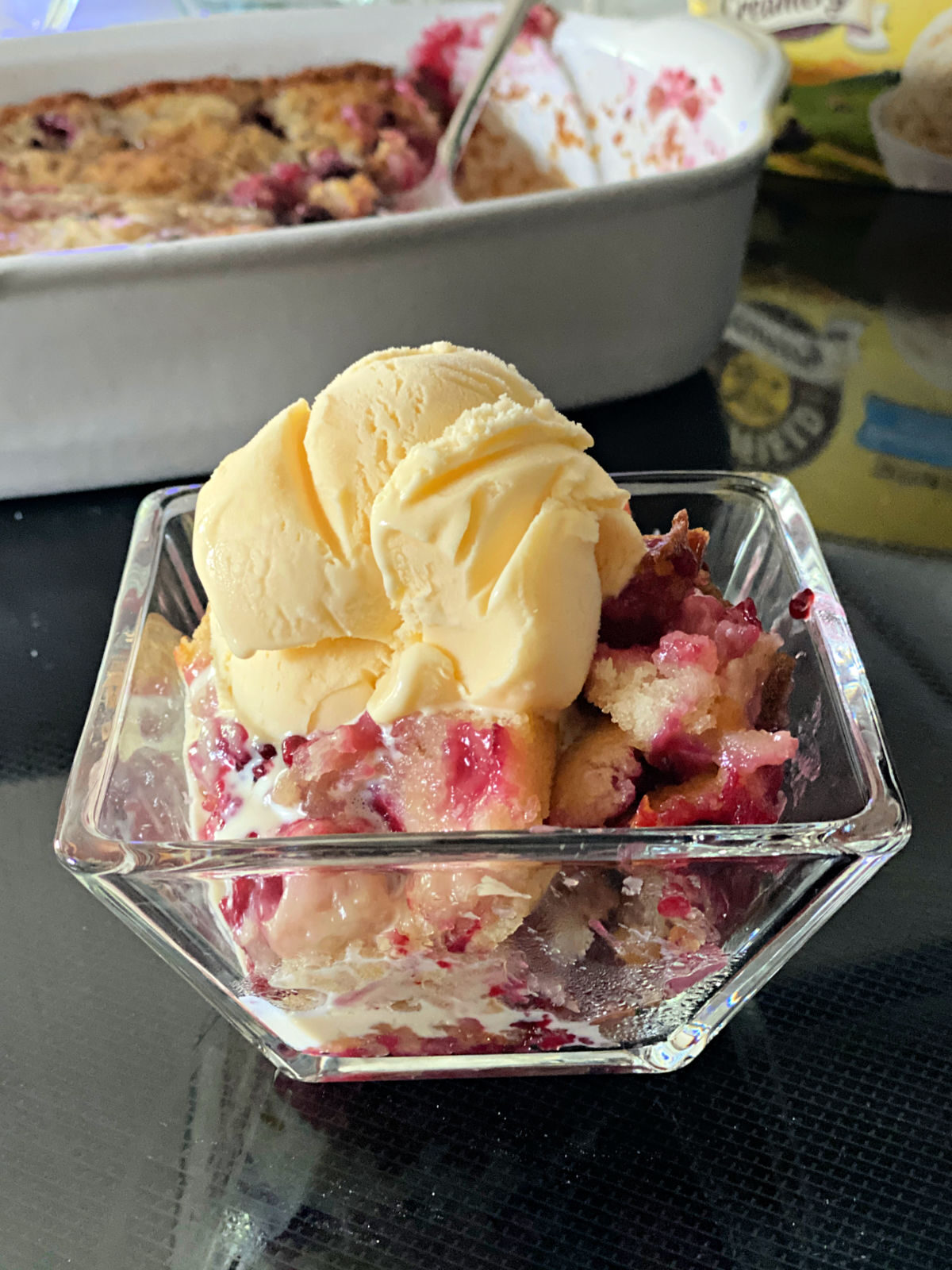 Glass bowl of blackberry cobbler topped with scoop of vanilla ice cream.