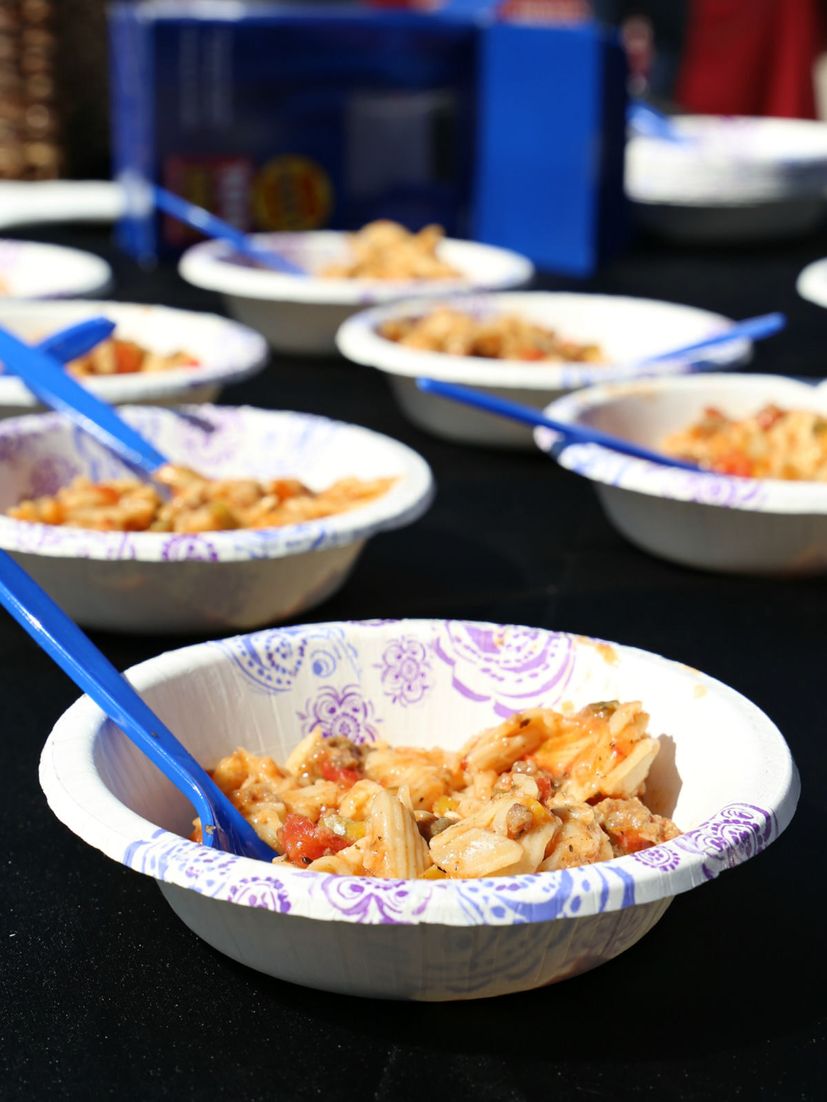 Paper bowls filled with brat stew and blue spoons.