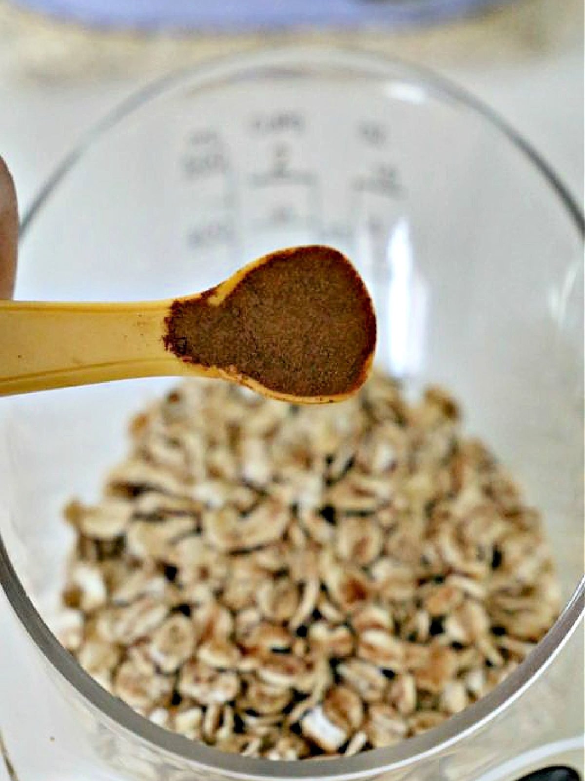 Teaspoon of cinnamon being poured into measuring cup with oats.