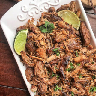 Platter with shredded pork carnitas and lime wedges.
