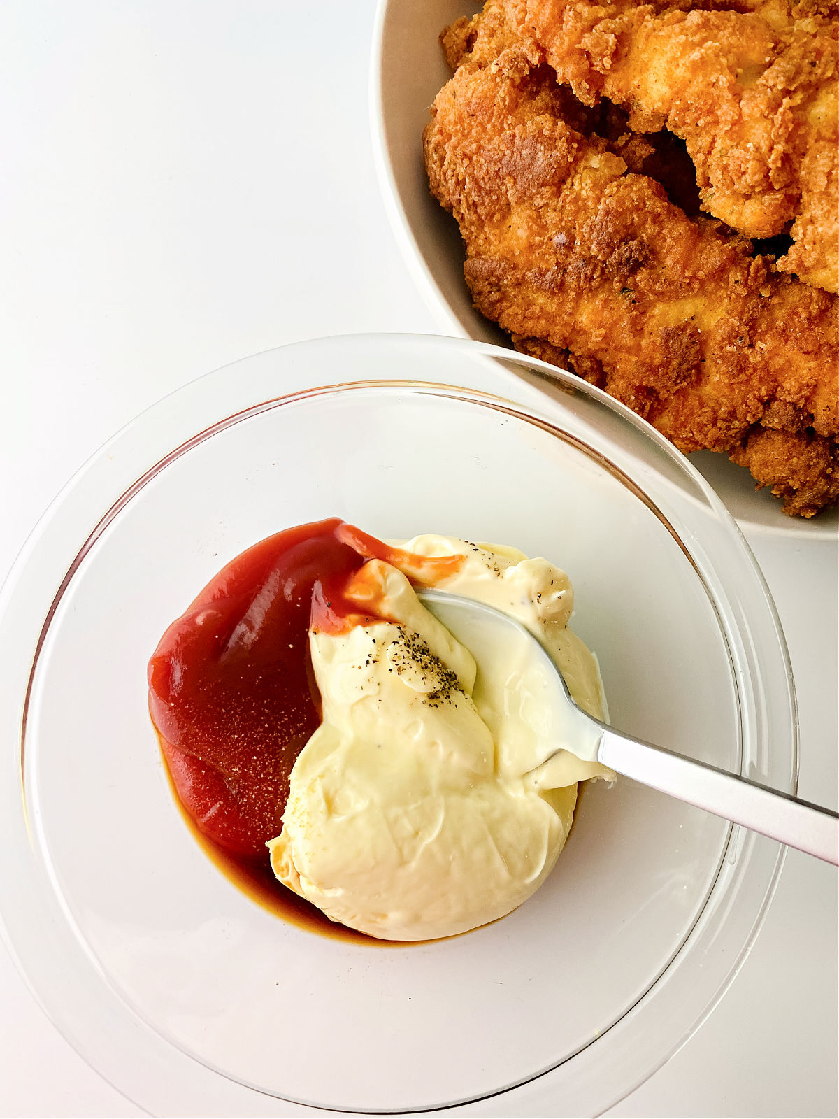 Mayonnaise and ketchup in a small glass bowl with a platter of chicken tenders.