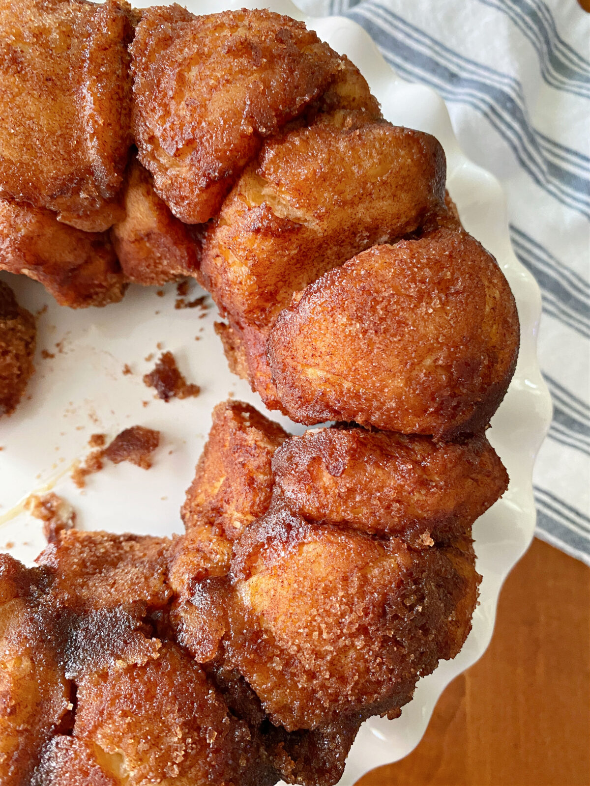 Monkey bread on a white cake plate surrounded by a blue and white tea towel.