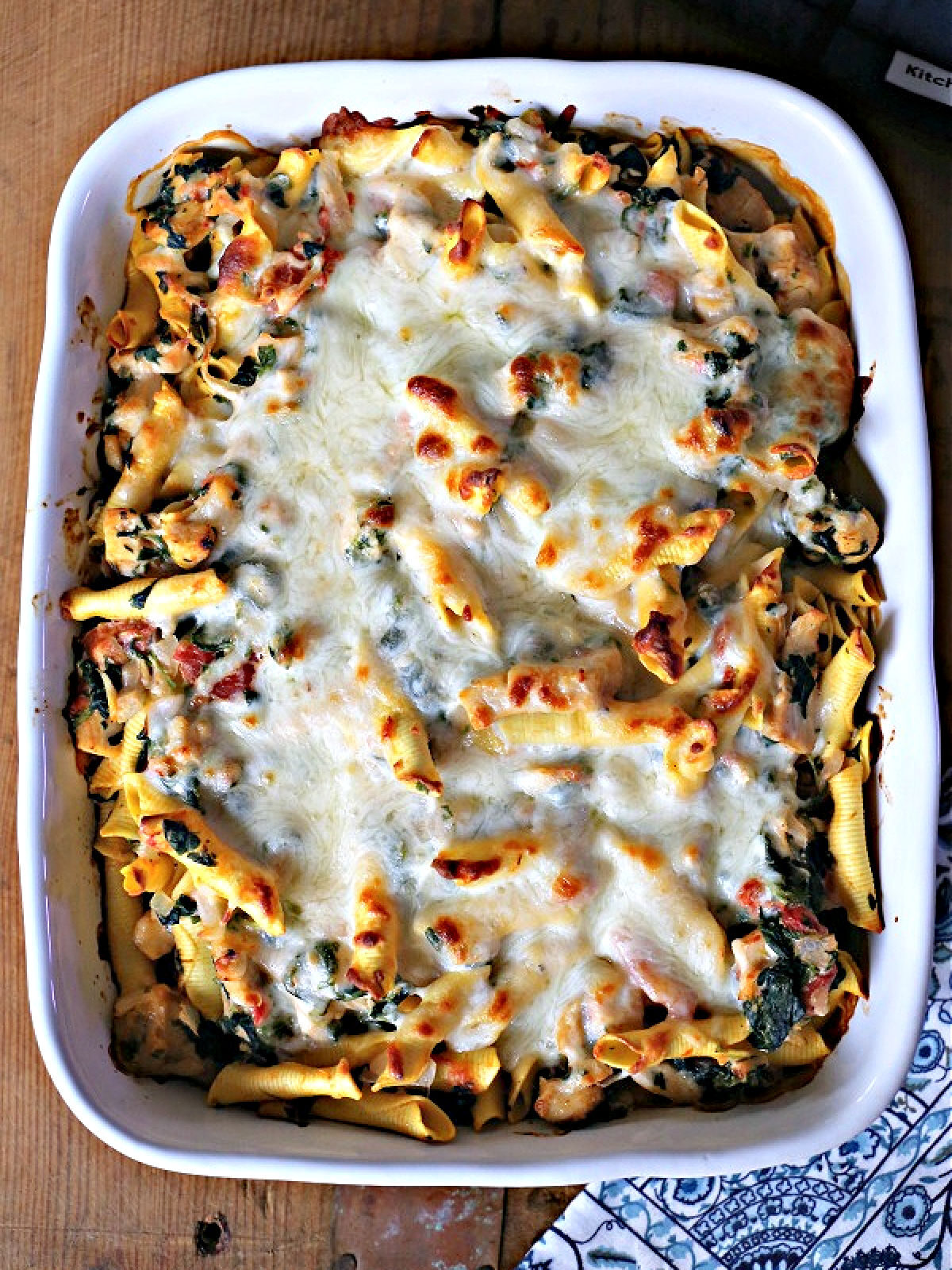 White casserole dish with pasta, chicken, cheese, and spinach.