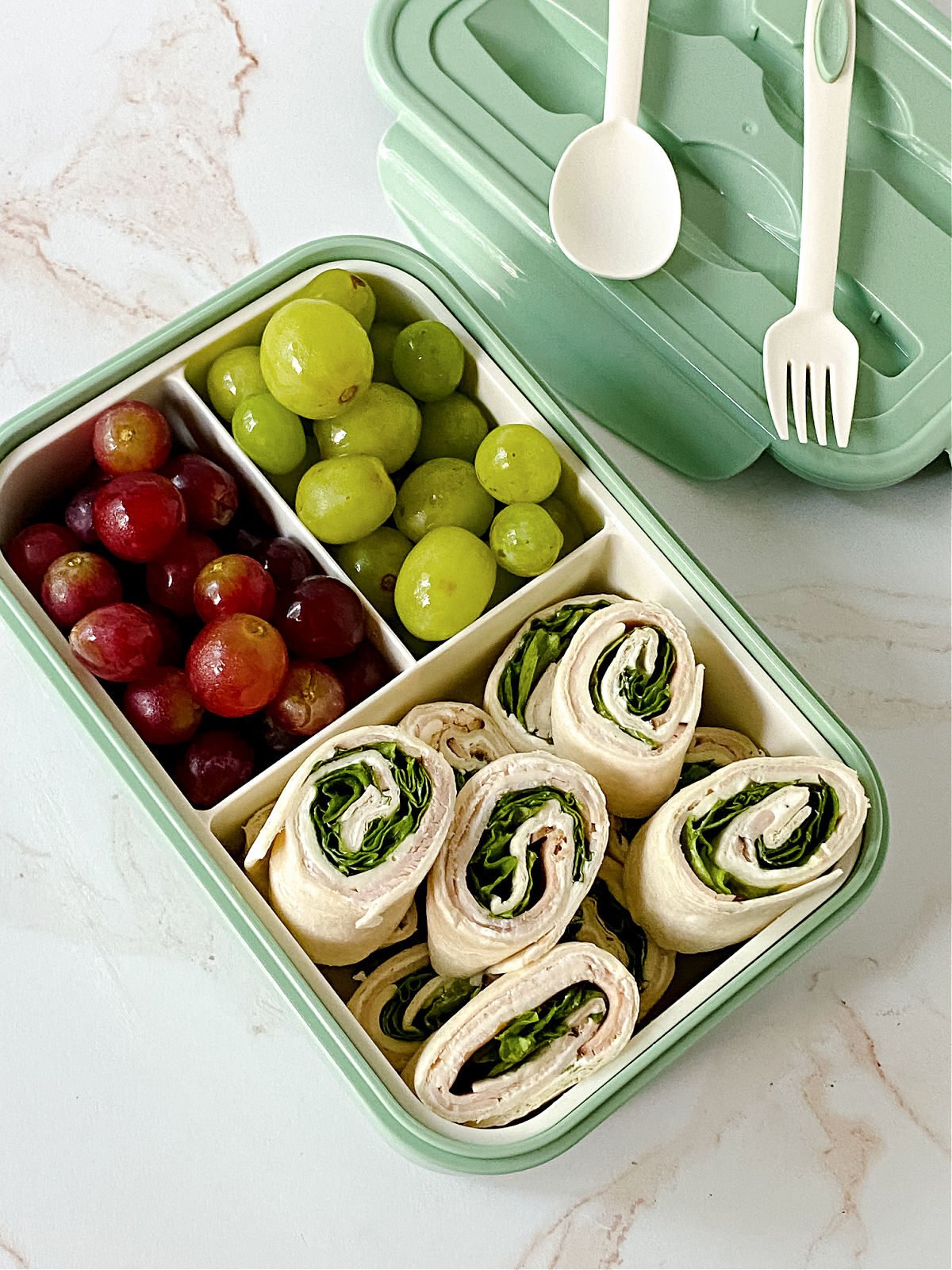 Pinwheel sandwiches and red and green grapes in a bento box.