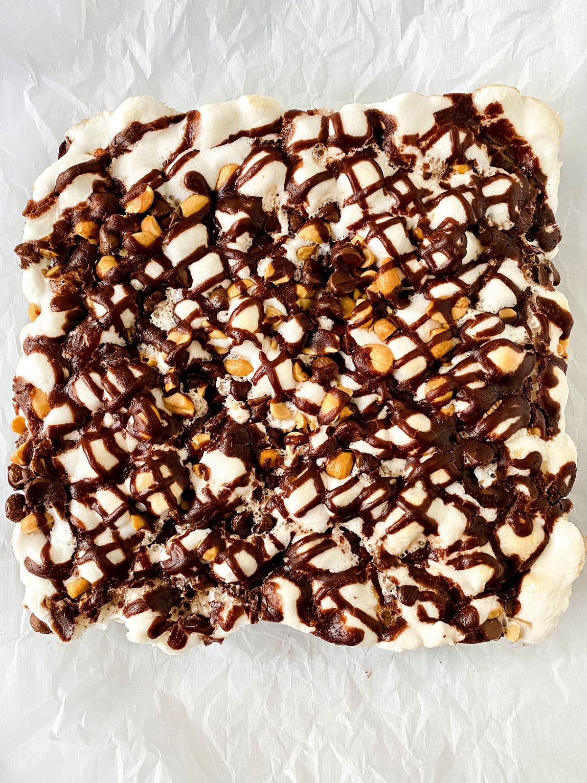 Rocky Road Brownies with peanuts, marshmallows, and chocolate drizzle on parchment paper.