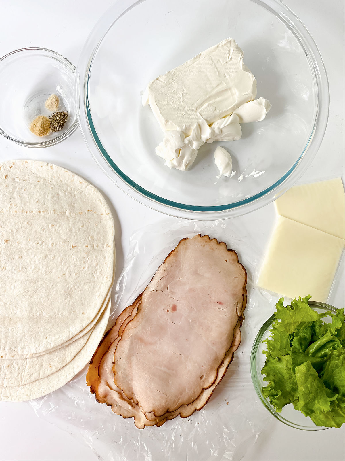 Flour tortillas, turkey, cheese, lettuce, cream cheese, and seasoning on a white background.