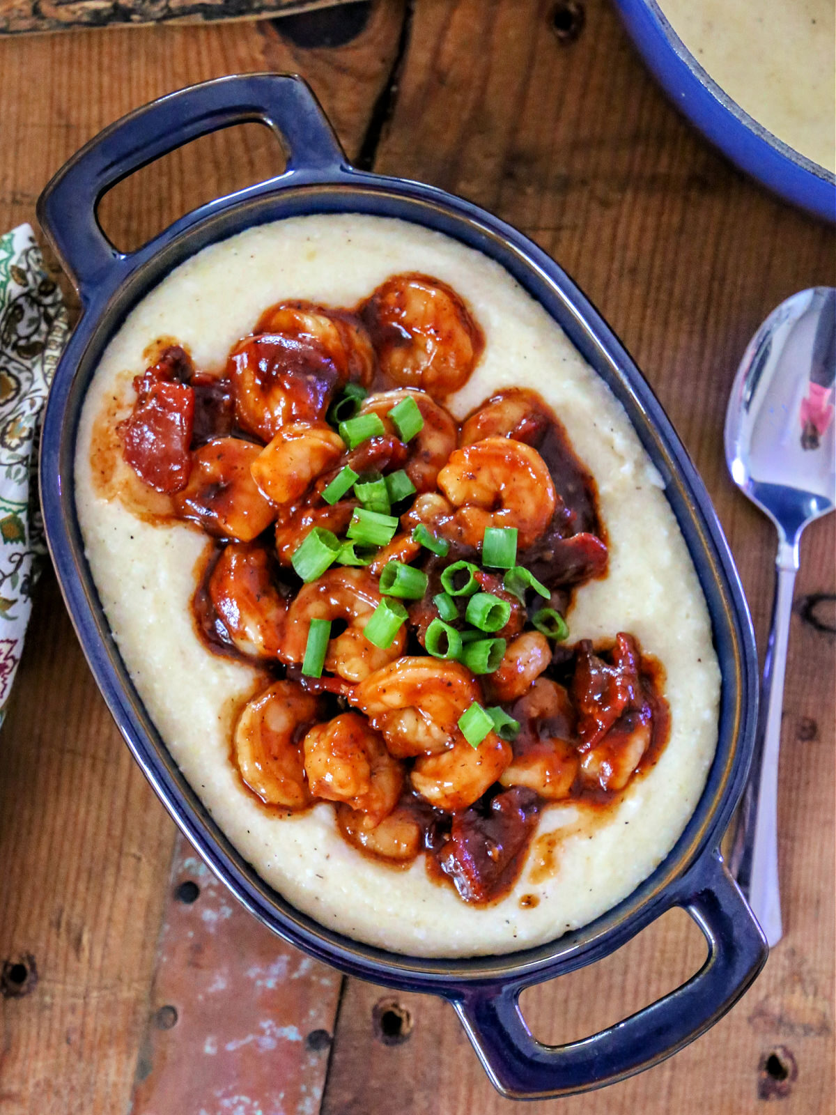 Blue dish filled cheesy grits topped with bbq shrimp and scallions.