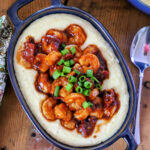 Blue dish filled cheesy grits topped with bbq shrimp and scallions.