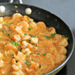 Non-stick skillet with shrimp scampi garnished with parsley.