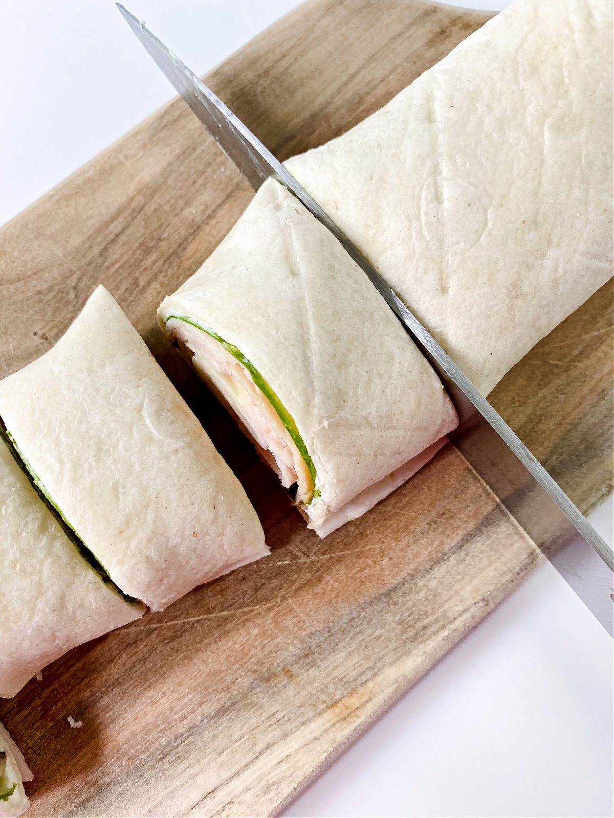 Knife cutting through a rolled pinwheel sandwich.