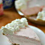 Slice of strawberry pie topped with whipped cream on a plate.