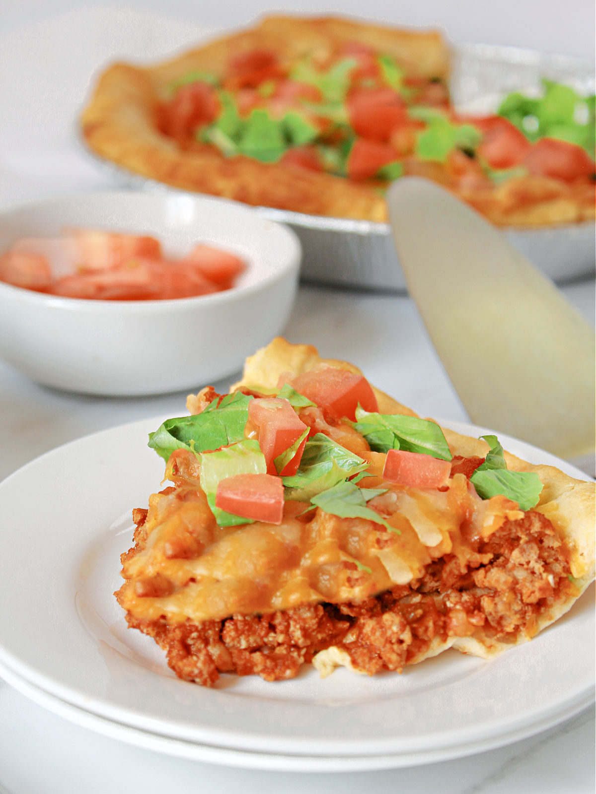 Slice of taco bake on white plates topped with lettuce and tomatoes.