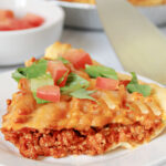 Slice of taco pie on a white plate topped with lettuce and chopped tomatoes.