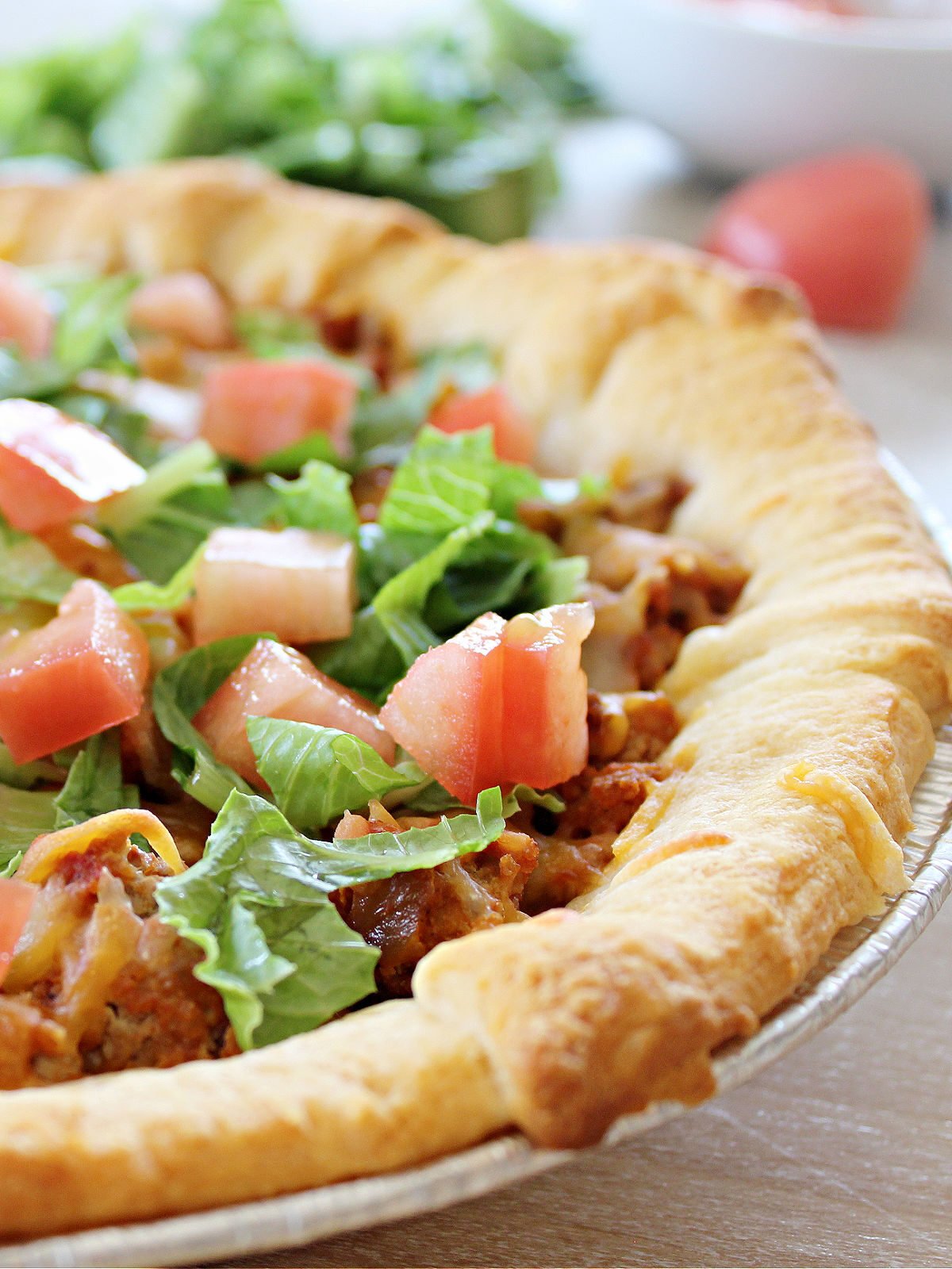 Taco pie made with ground beef and topped with layer of cheese and lettuce and tomatoes.