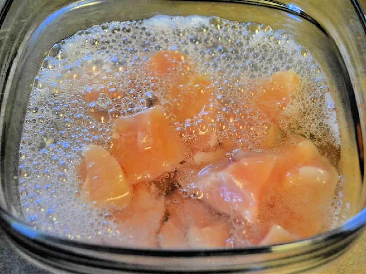 Chicken nuggets in a brine in a glass bowl.