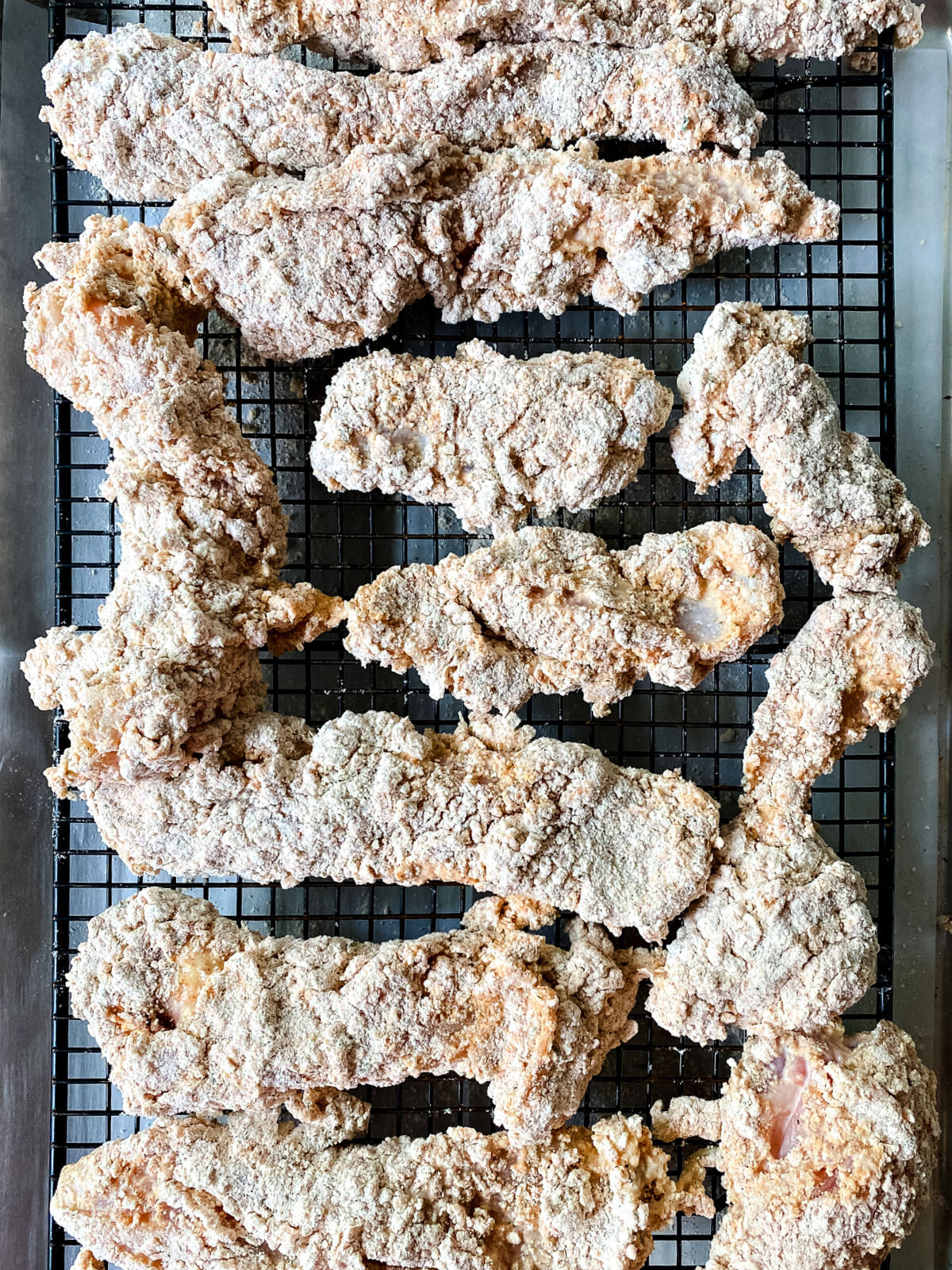 Chicken tenders dredged in flour on a black wire rack.
