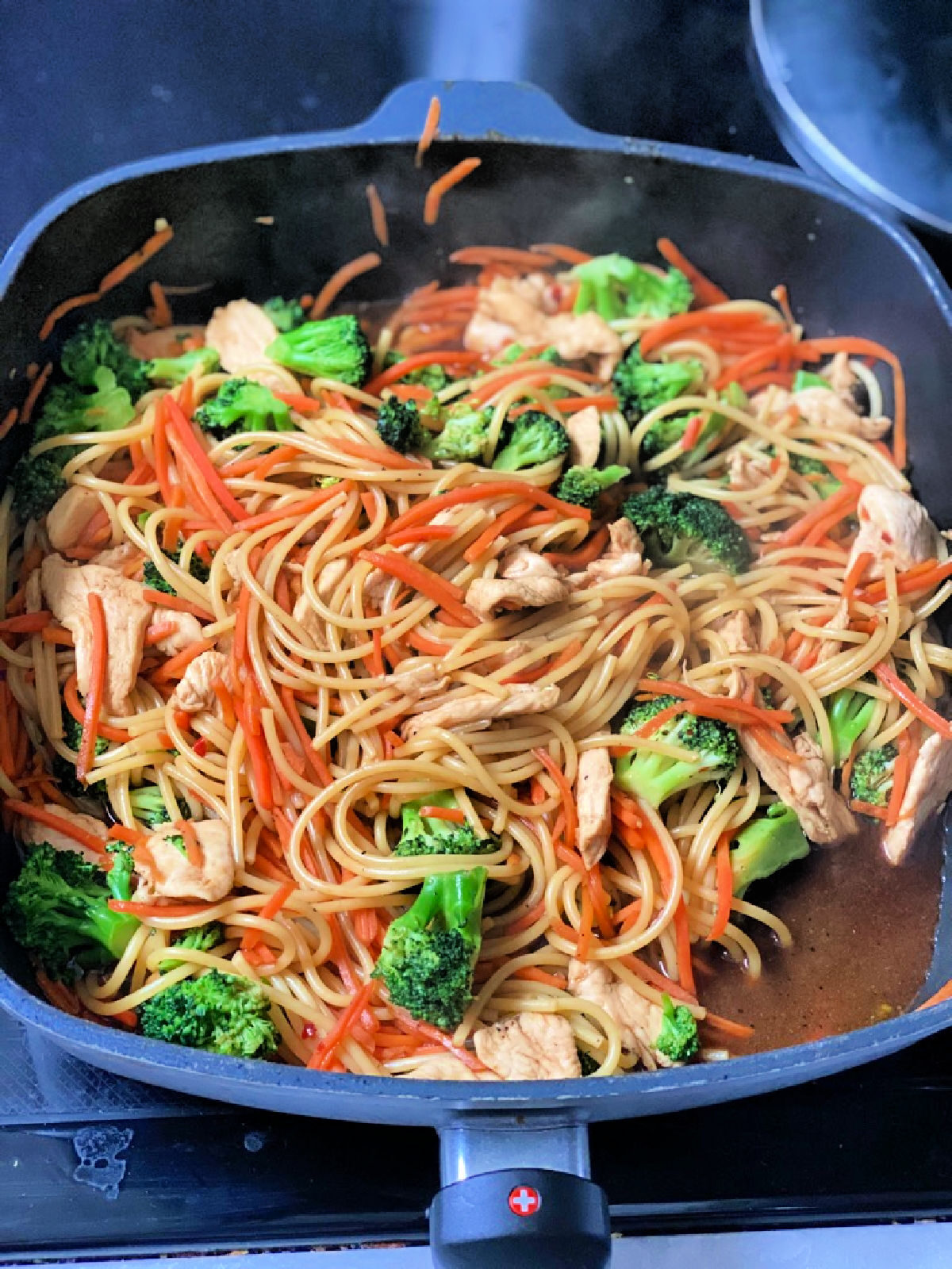 Spaghetti noodles, lo mein seasoning, broccoli, and shredded carrots in a skillet.