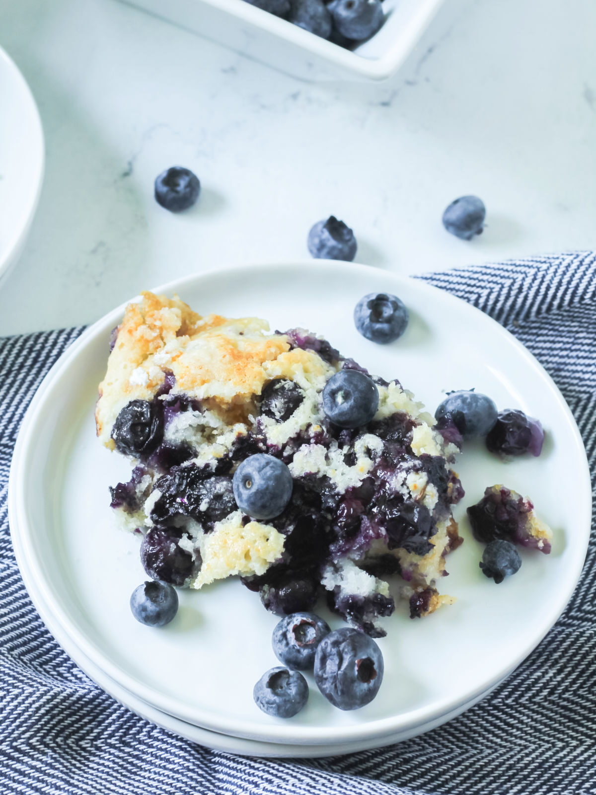 Blueberry cobbler topped with fresh blueberries on a white plate.
