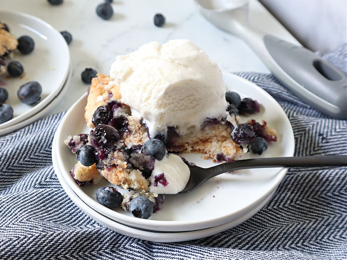 Blueberry cobbler and scoop of ice cream on white plate with spoon.