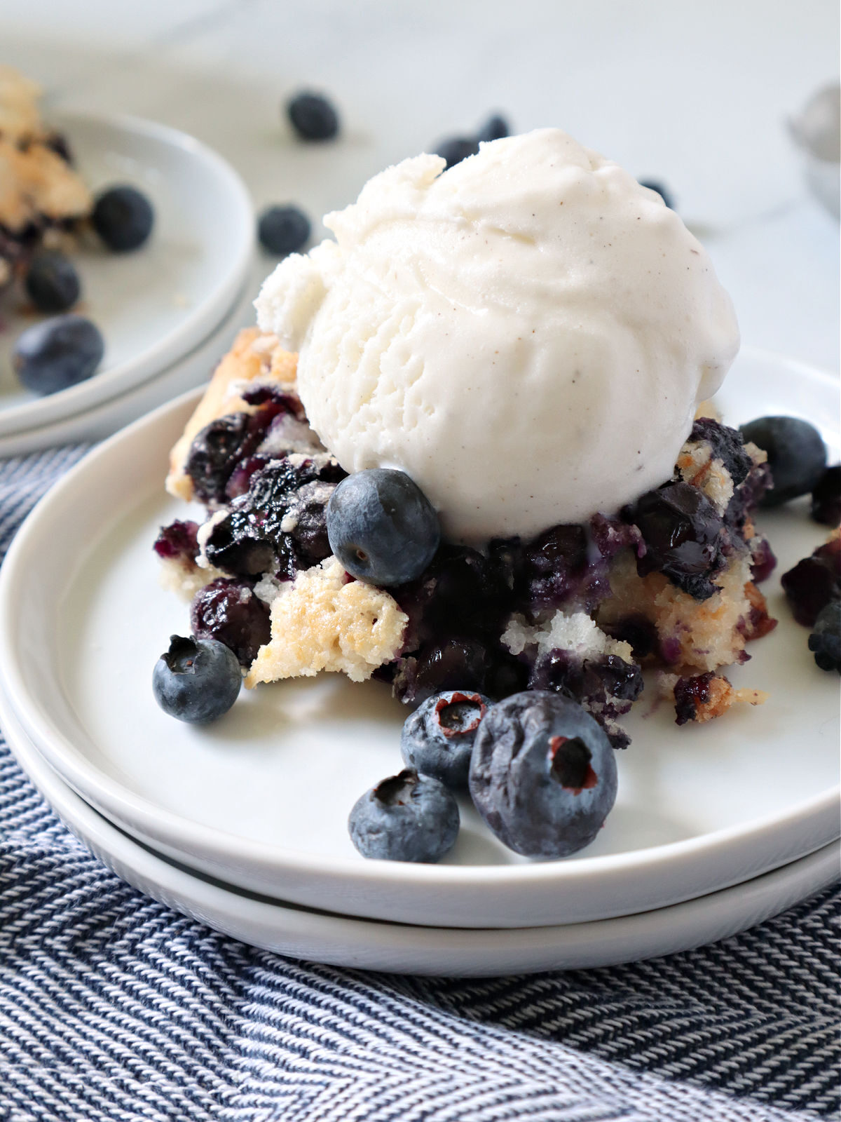 Scoop of vanilla ice cream on top of blueberry cobbler on a white plate.